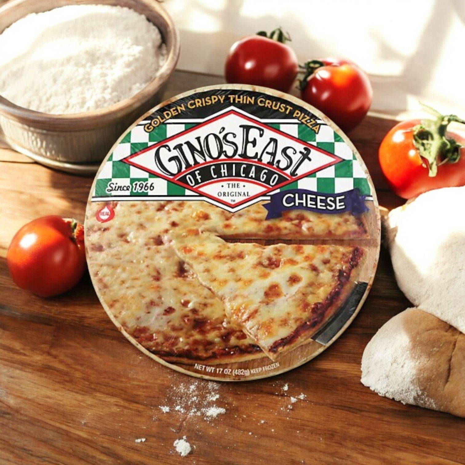 Gino's East Pizza Golden Crispy Thin Crust Pizza – 15.6 oz sits on a wooden surface surrounded by tomatoes, flour, and dough, showcasing the mouthwatering flavor of classic Chicago thin crust pizza.