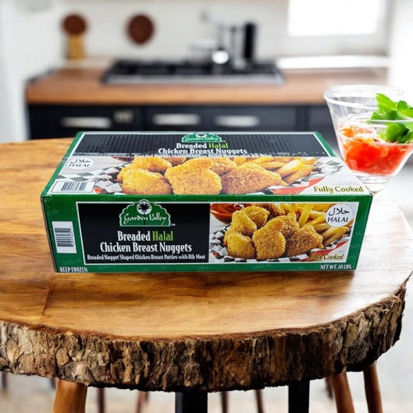 A box of Restaurant Depot Breaded Halal Chicken Breast Nuggets (10 lb) sits on a wooden table, featuring Halal-certified chicken, with a glass bowl of salad nearby in a cozy kitchen setting.