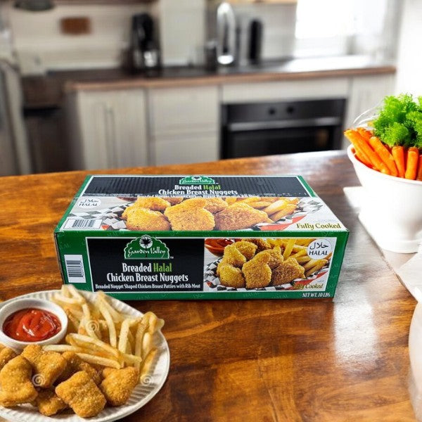 A box of Restaurant Depot Breaded Halal Chicken Breast Nuggets (10 lb) sits on a wooden table beside a plate of nuggets, fries, ketchup, and vegetables in a cozy kitchen.