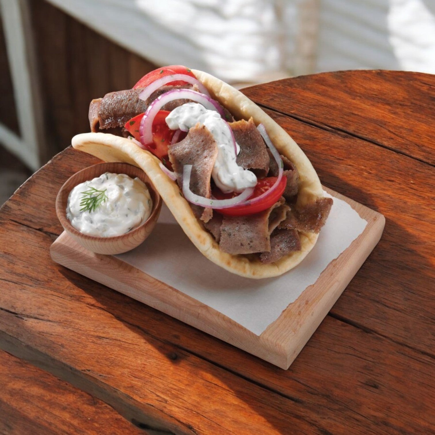A gyro sandwich made with Devanco Foods Halal Gyro Slices (beef and lamb), onions, tomatoes, tzatziki sauce on pita bread, served with a side of sauce and Mediterranean spices. Brand: Devanco.