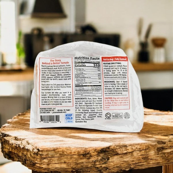A package of Padrino Tamales Pork Tamales (60 oz, 3 Count) with nutrition facts, ingredients, and heating directions on the back sits on a rustic wooden table—hand-rolled in corn husks, ideal for foodservice distributors.