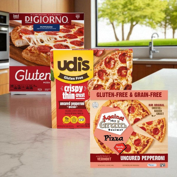 Three boxes of Easy Lunches Gluten-Free Pepperoni Pizza Assortment – DiGiorno, Against The Grain & Udi’s – are shown on a kitchen counter with a window and greenery in the background.