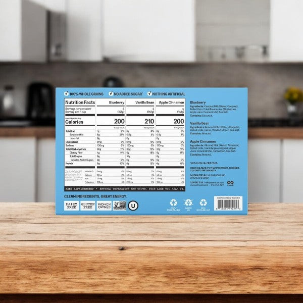 A Mush Overnight Oats Variety Pack box (12-count, 5 oz each) sits on a wooden counter in a modern kitchen, displaying nutrition facts, ingredients, and its dairy-free recipe.