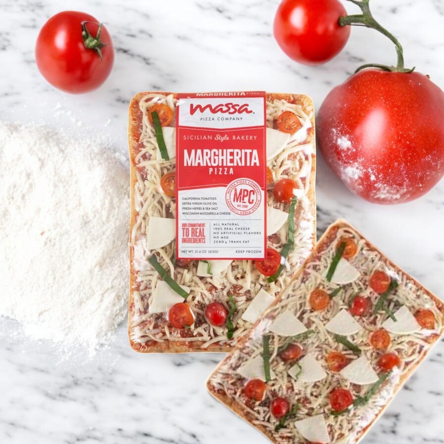 Massa Pizza Co. Margherita Bakery Pizza, 21.6 oz., by Massa Pizza sits on a marble surface, surrounded by three fresh tomatoes and a pile of flour—perfect for enjoying authentic Italian pizza flavor at home.