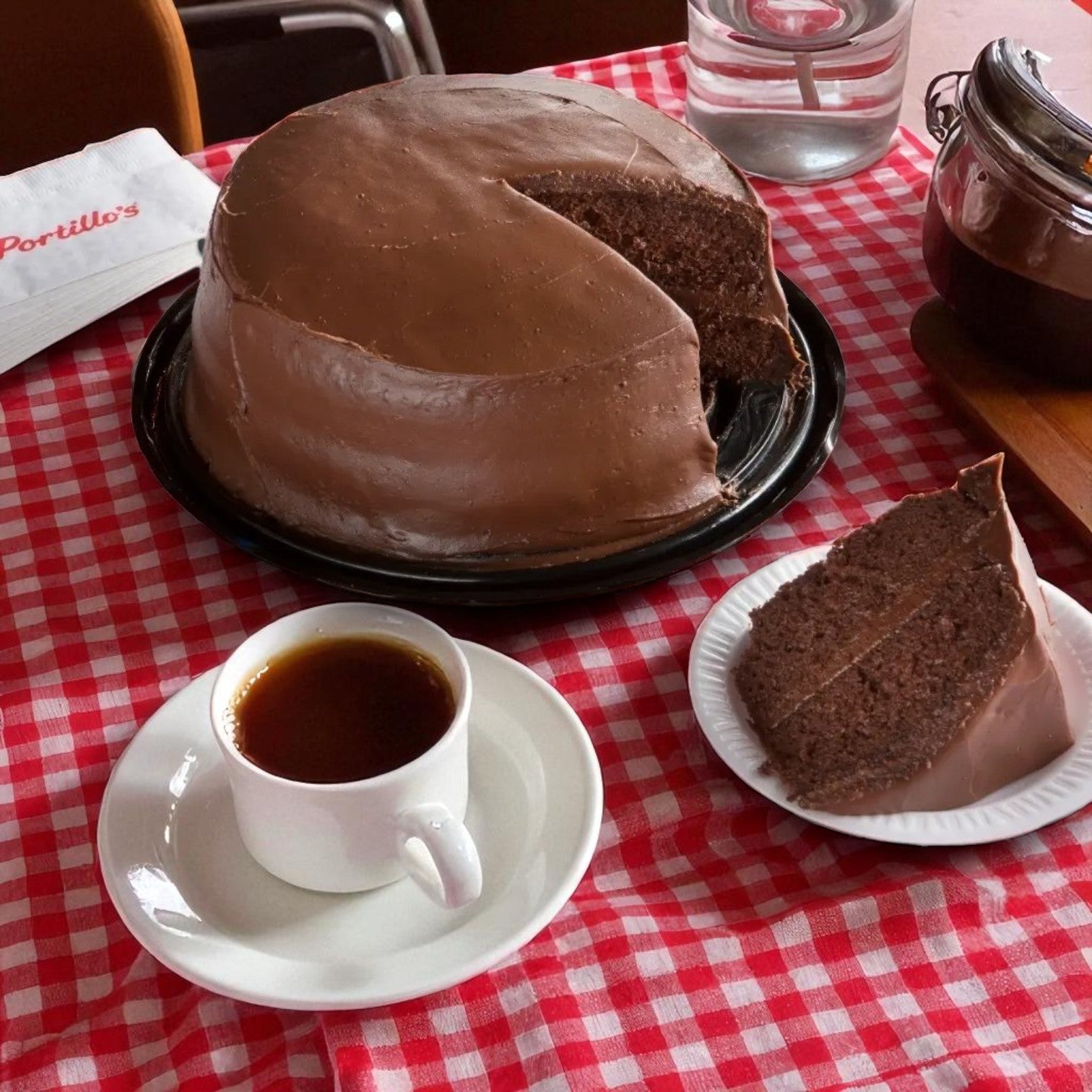 Portillo's Famous Chocolate Cake & Garrett Popcorn Garrett Mix Combo by Garrett is served with a slice on a white plate and coffee, all on a red checkered tablecloth—a classic Chicago dessert pairing.