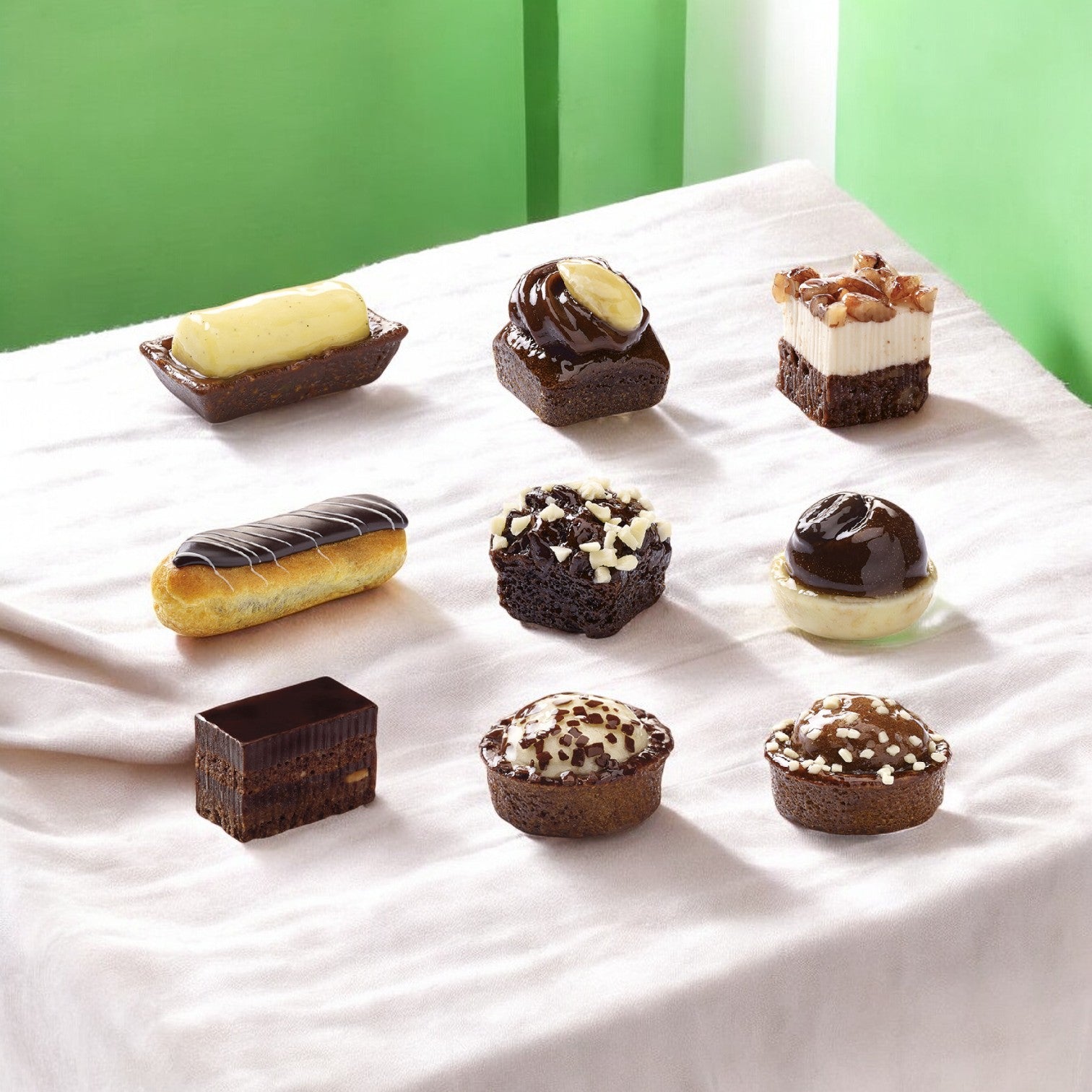 Enjoy the Pasquier Cake Assortment with a beautiful selection of French pastries and desserts in a 3x3 grid on a white cloth. The Petits Fours Black & White, featuring 48 pieces, are exquisite creations of sweet elegance.