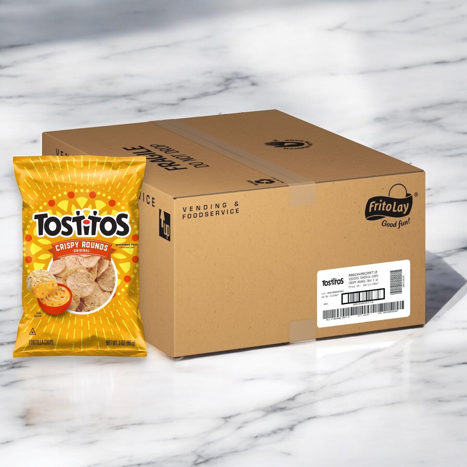 A pack of Tostitos Tortilla Chips, Round – 28 Pack (3 oz Each) by Tostitos sits beside a sealed Frito-Lay shipping box on a marble surface, ready for your next dipping snack.