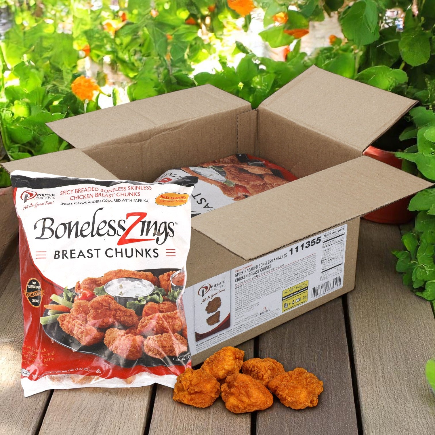 A bag of Pierce Boneless Zing Chicken Wings, Breaded & Precooked – 2/5 LB Bags, is shown beside an open box with more bags and chicken pieces on a wooden surface, set against flowering plants in the background.