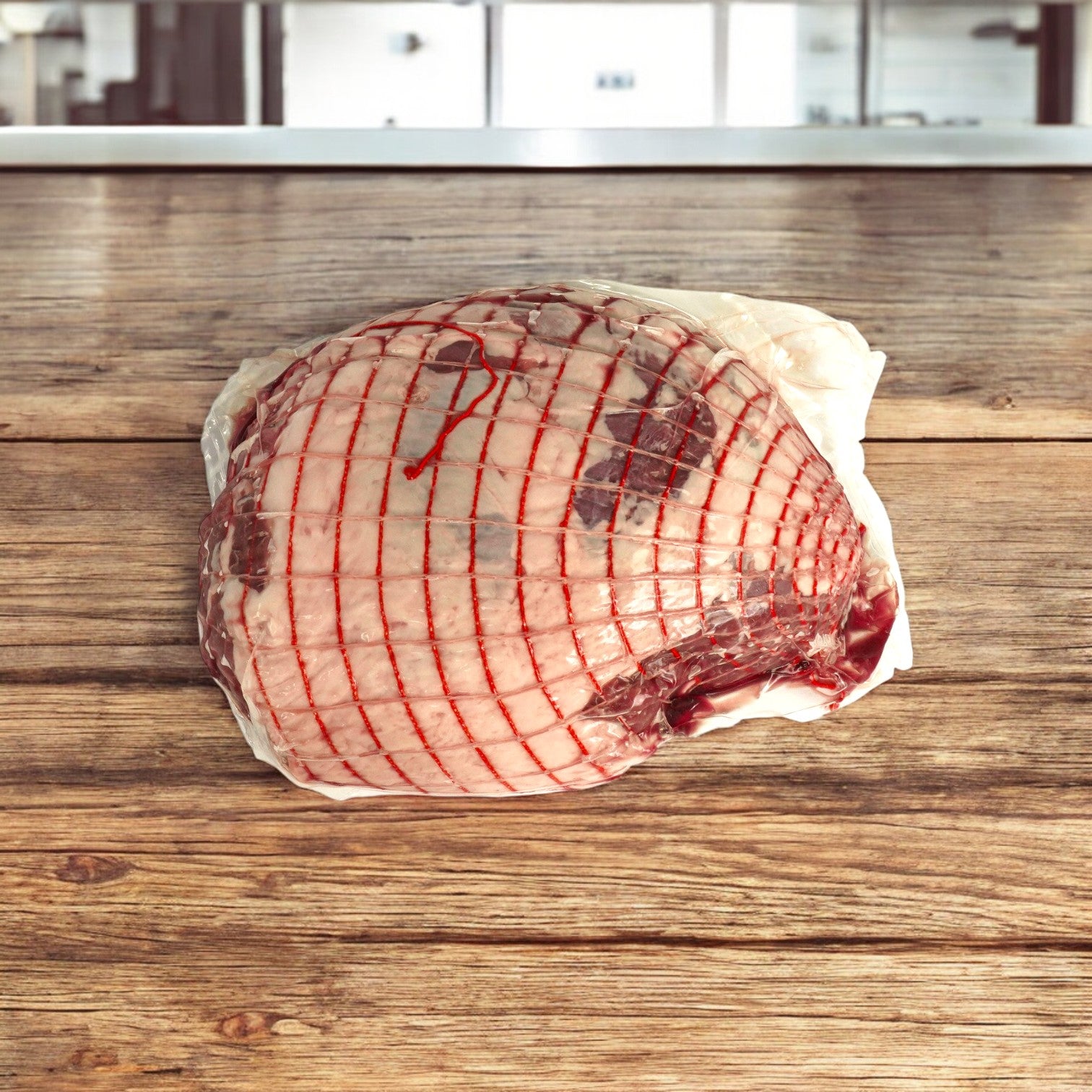 A Butchers Block Boneless Halal Lamb Leg – Frozen (5/6 lb avg, 26 lb avg) rests on a wooden surface in a kitchen.