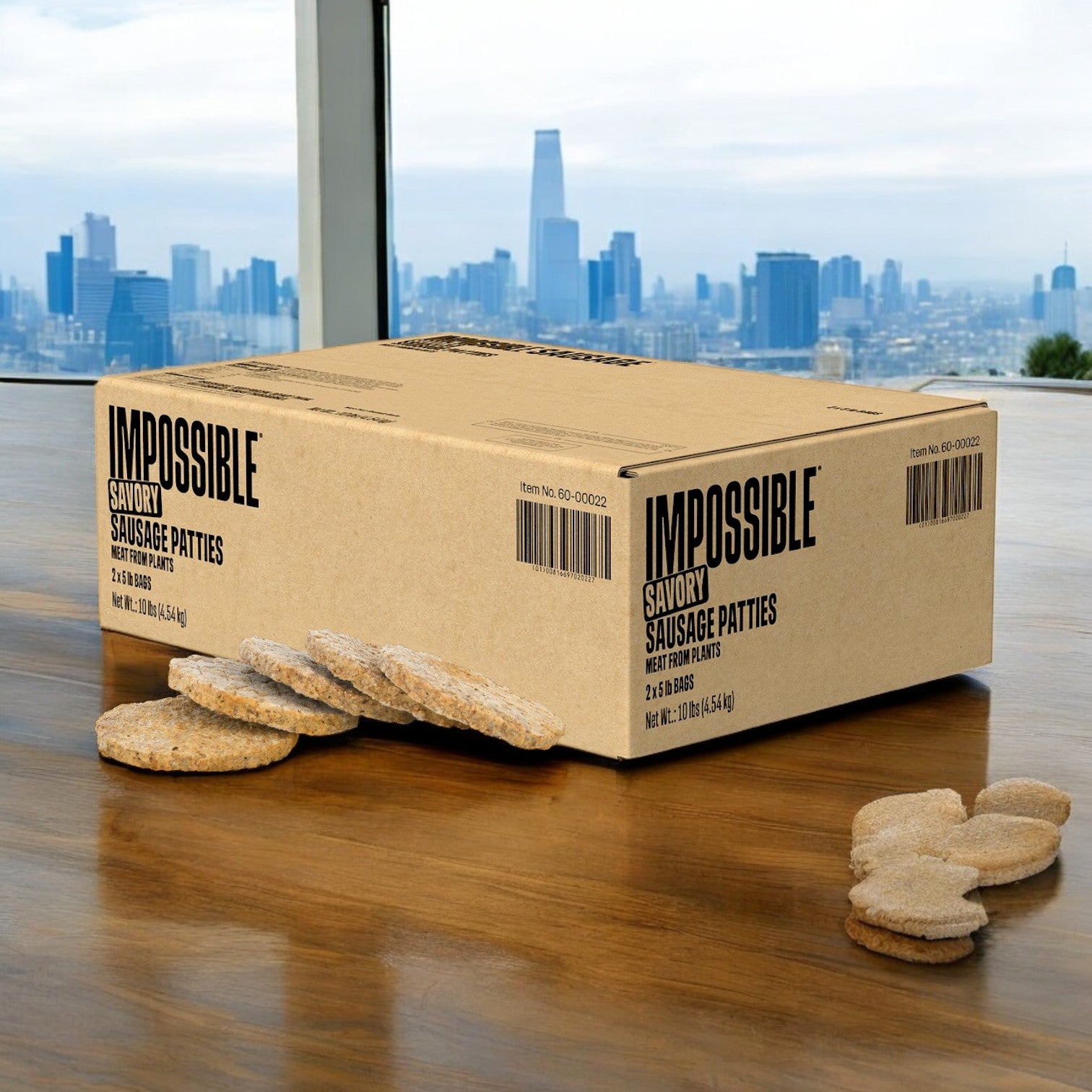 A cardboard box labeled "Impossible Foods Sausage Patty Impossible 2/5 LB-1.6 oz each" by Impossible Foods sits on a wooden table with several plant-based sausage patties nearby; a city skyline is visible through the windows in the background.