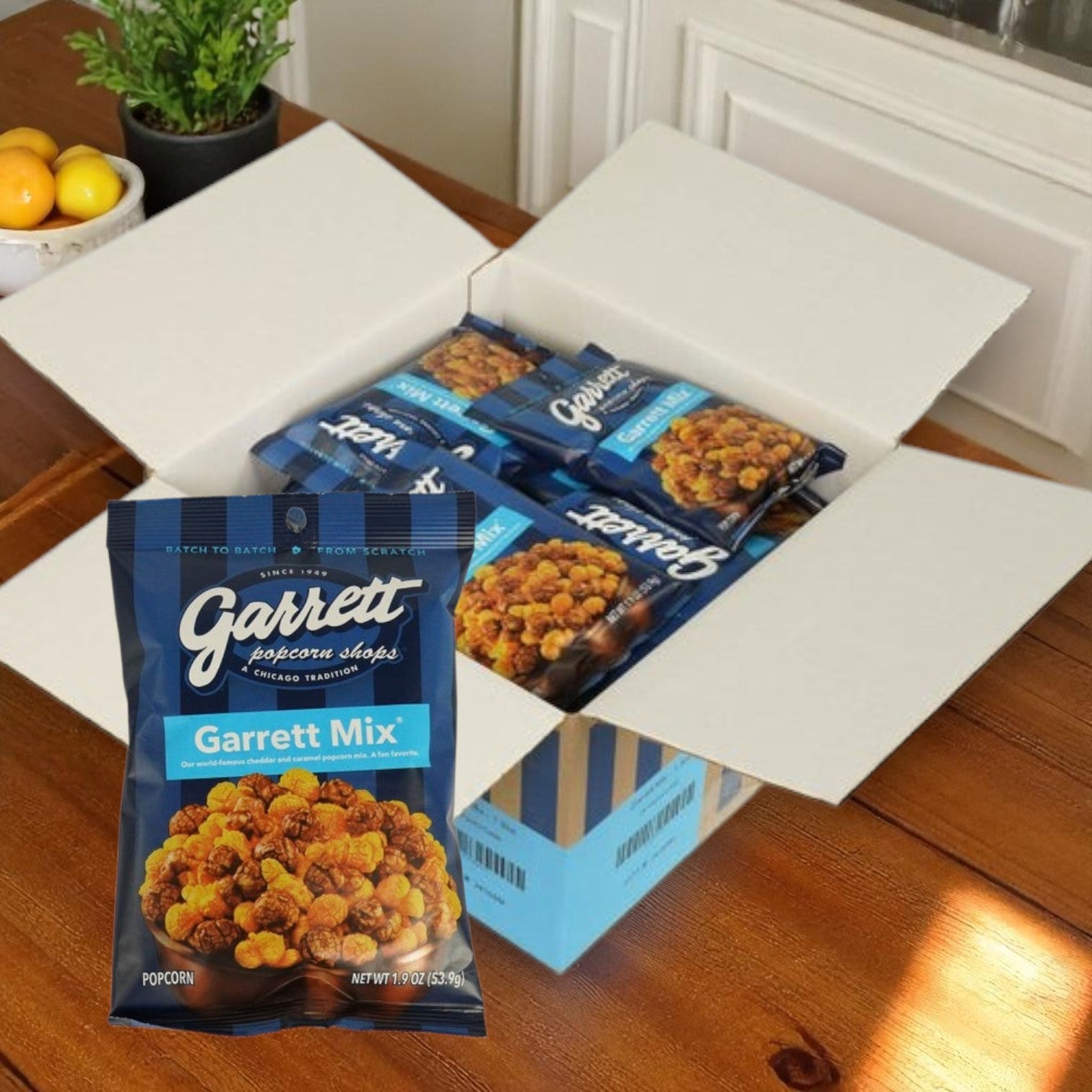 An open box of Garrett Brands Snack Popcorn – Garrett Mix®, 1.9 oz Bags (24-Pack) sits on a wooden table, with a close-up of one bag in the foreground showcasing the signature Chicago-style popcorn from Garrett.