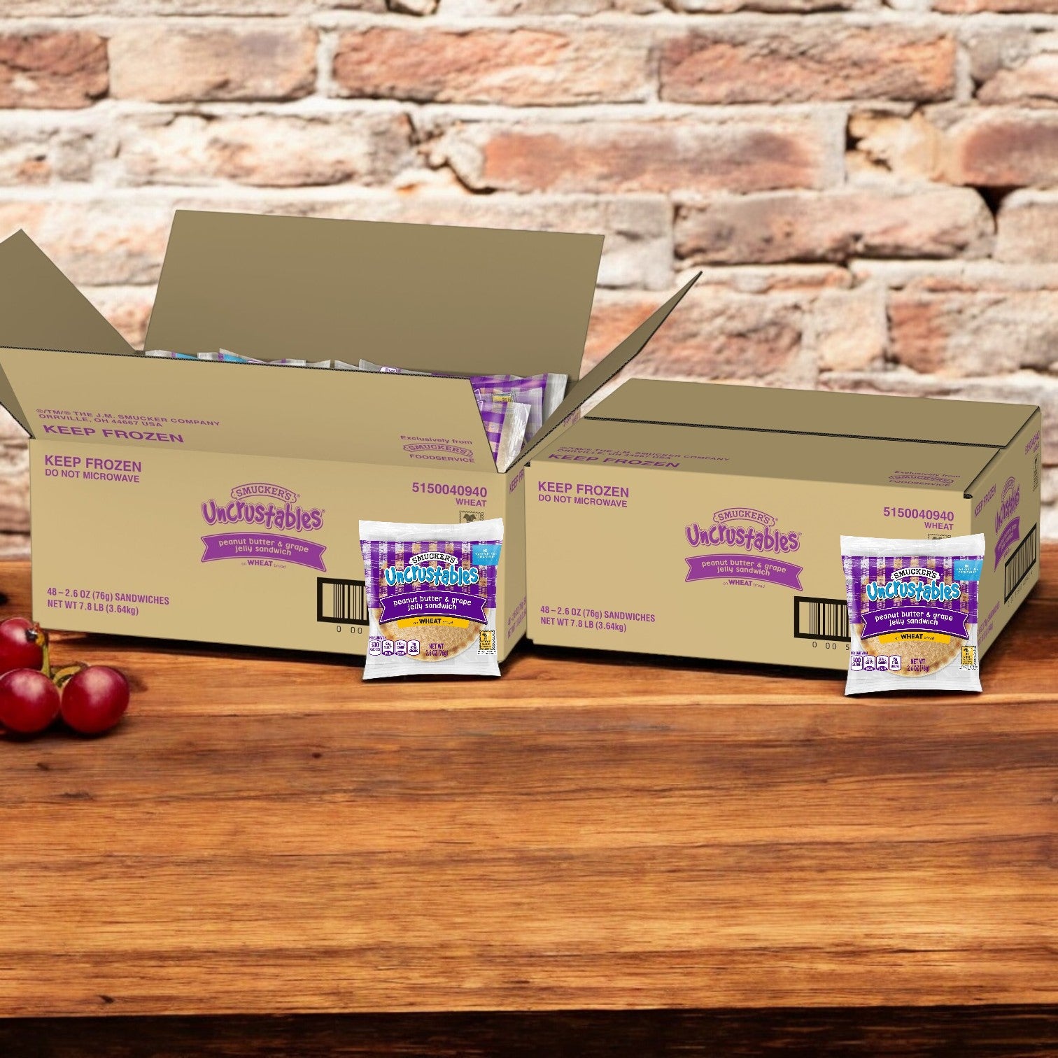 Two open boxes of Smucker's Uncrustables Peanut Butter & Grape Jelly Wheat Sandwiches rest on a wooden surface with two apples against a brick wall. Enjoy the classic combo for a delicious snack anytime.