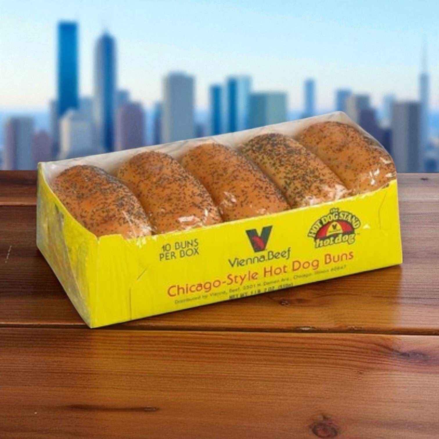 A Vienna Beef Hot Dog Kit – Frankfurters + Poppy Seed Buns sits on a table, with the famous poppy seed buns prominently featured and a blurry city skyline in the background.