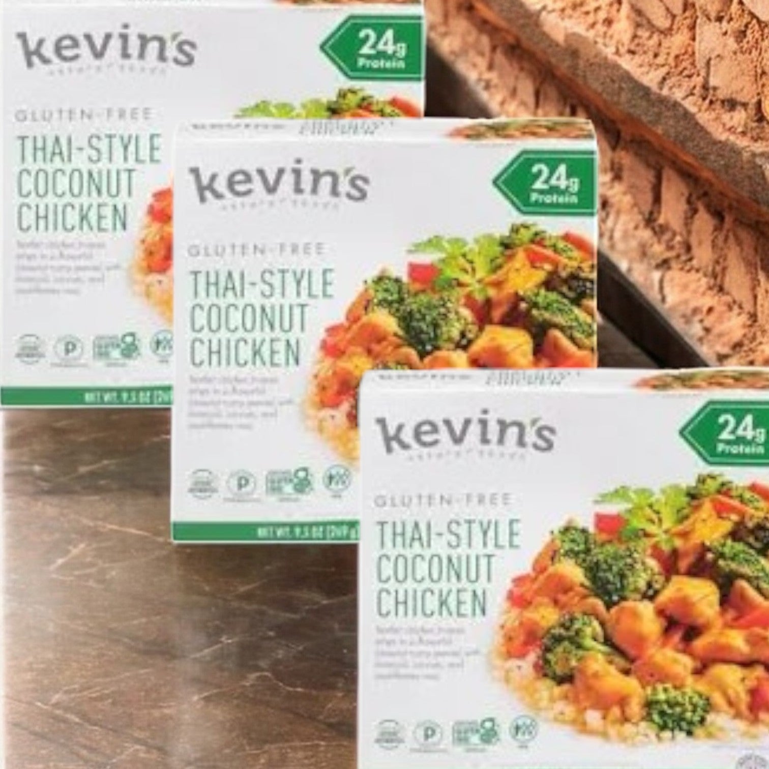 Three boxes of Kevin's Natural Foods Thai-Style Coconut Chicken - 3 Count, a paleo-friendly and gluten-free meal from Kevin's, each with 24g of protein, are displayed on a counter.