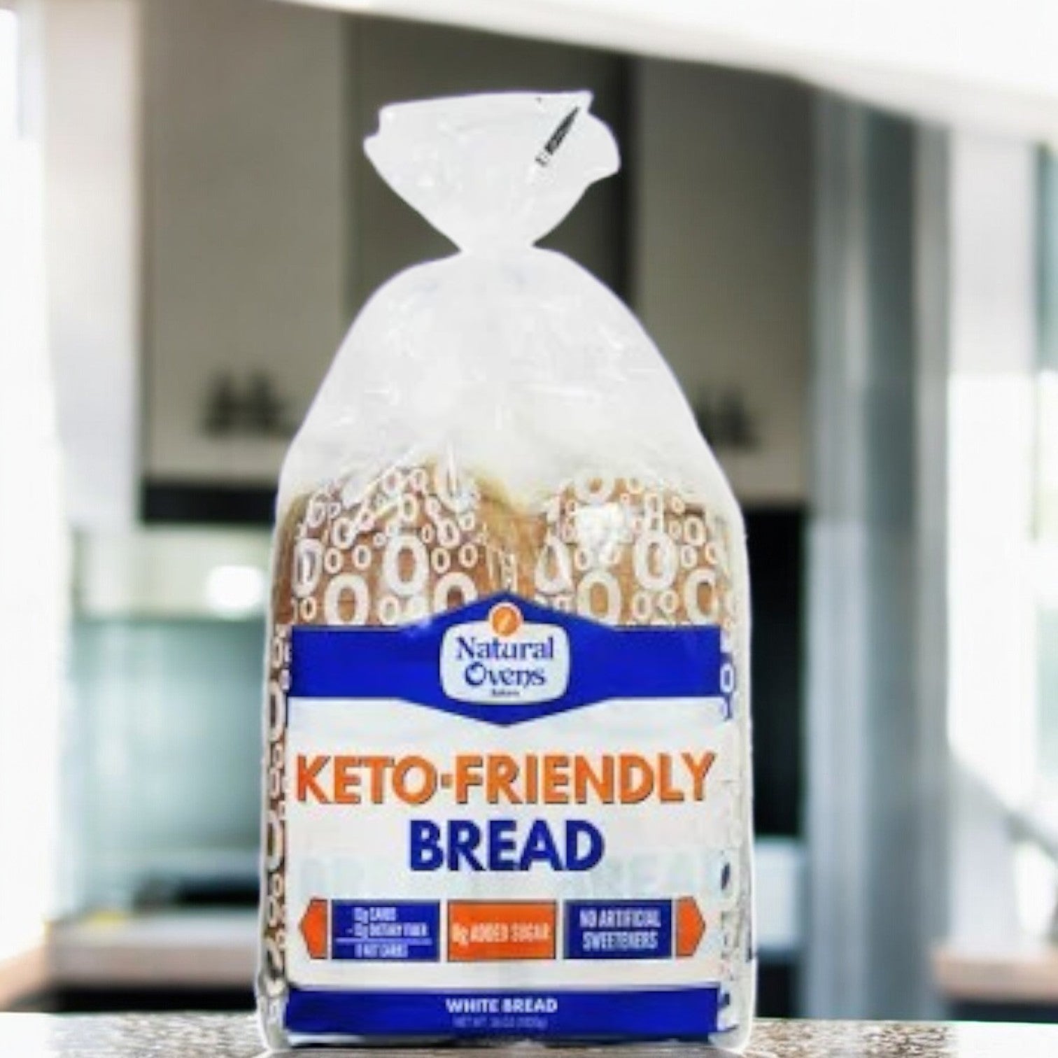 A loaf of Natural Oven's Keto Friendly Bread-1 Count sits on a kitchen counter in a plastic bag—ideal for a low-carb or keto diet, with no added sugar or artificial sweeteners, by Natural Oven's.