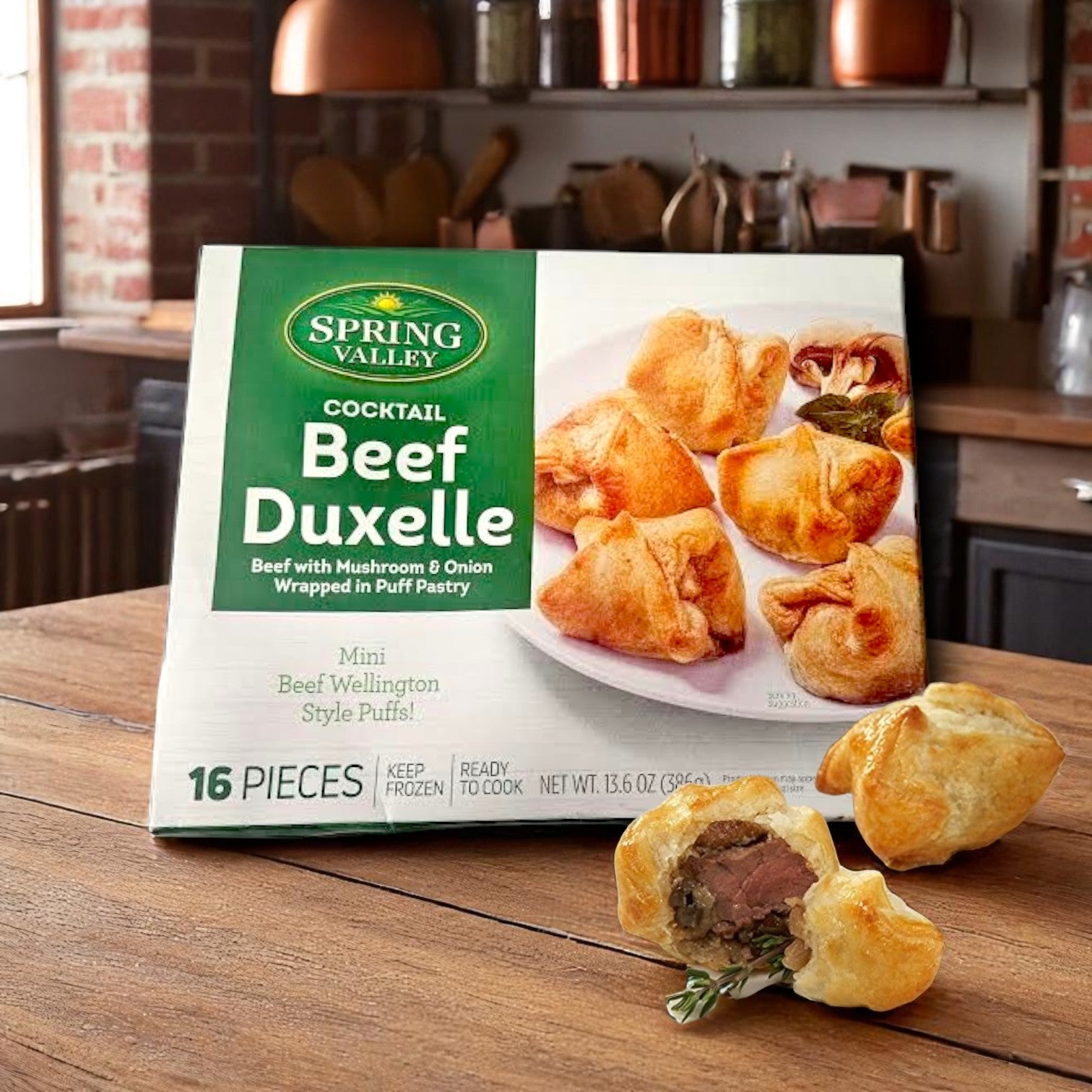 A box of Spring Valley Cocktail Beef Duxelle Mini Beef Wellington Style Puffs (16 pieces, 13.6 oz) sits on a wooden counter, with two cooked puffs—one cut open—showing flaky pastry and mushroom duxelle filling.