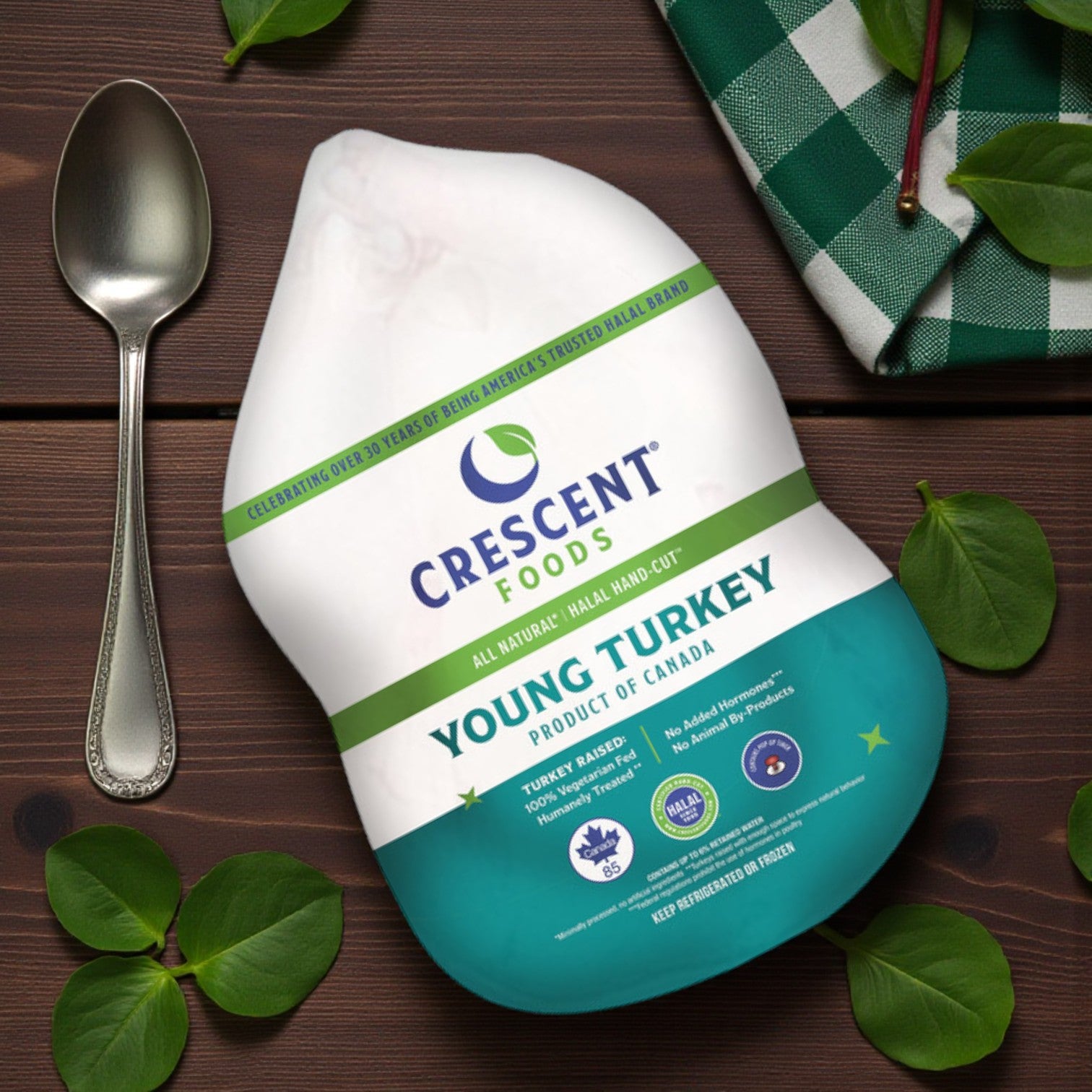 A Crescent Foods All-Natural Halal Young Turkey (frozen, 12-14 lbs) sits on a table with a spoon, green leaves, and a checkered napkin. The packaging shows product info and certifications.