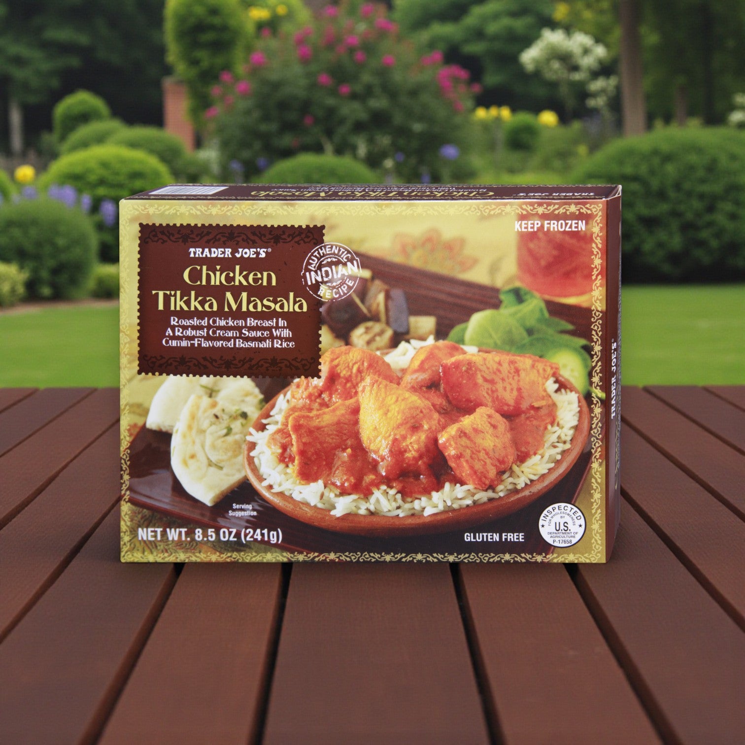 A box from Easy Lunches’ Trader Joe’s Indian Cuisine Combo – 3 Pack Variety is displayed on a wooden table outside, with a garden in the background.