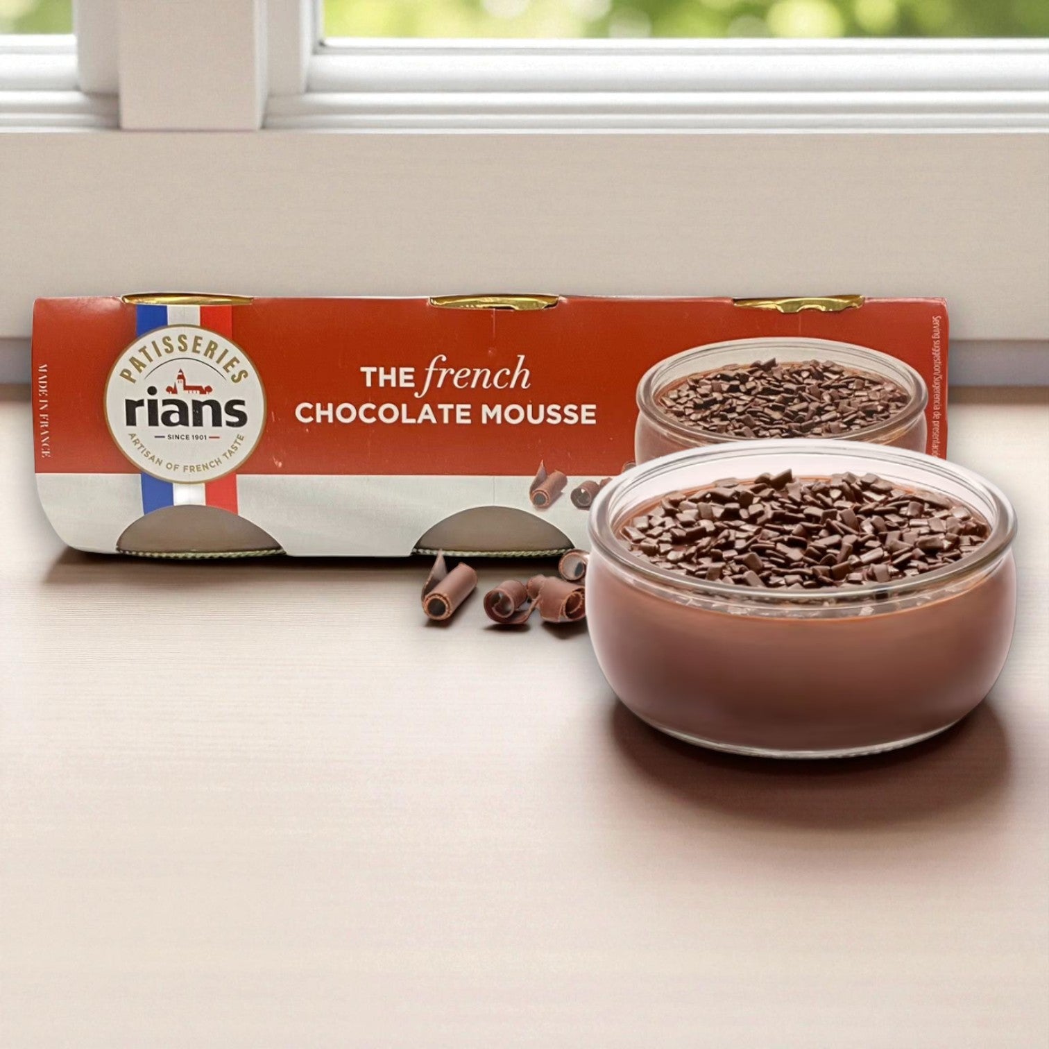 A glass bowl of rich chocolate mousse sits in front of Rian's packaging labeled "Rians French Chocolate Mousse, 3.17 oz Cups, 6 Pack," highlighting this classic French dessert from Rian's.