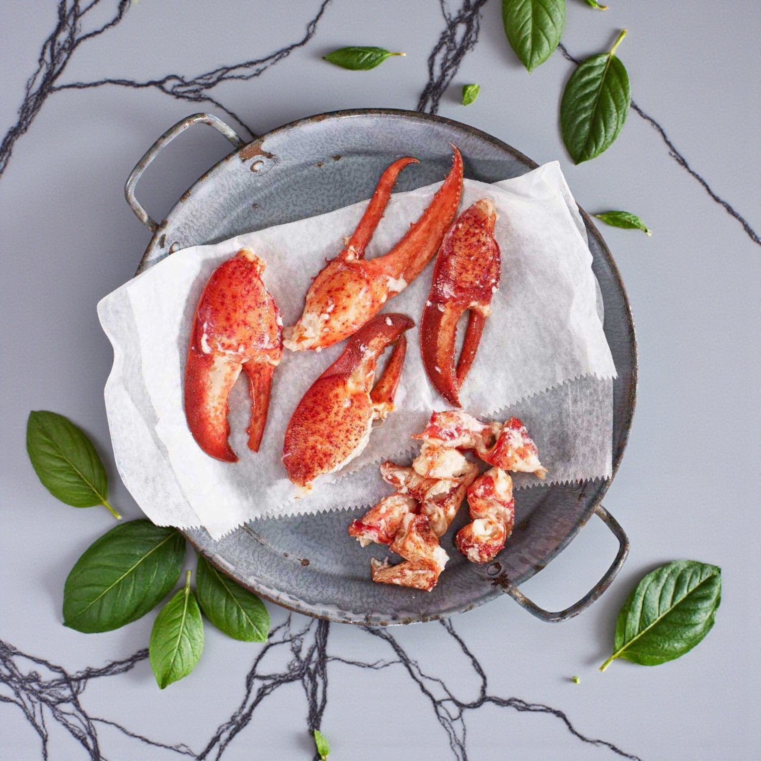 A metal tray with Easy Lunches Maine Lobster Meat Claw and Knuckle—(2) 2 lb portions, 4 lbs total—served on parchment paper and surrounded by green leaves on a gray marble surface.