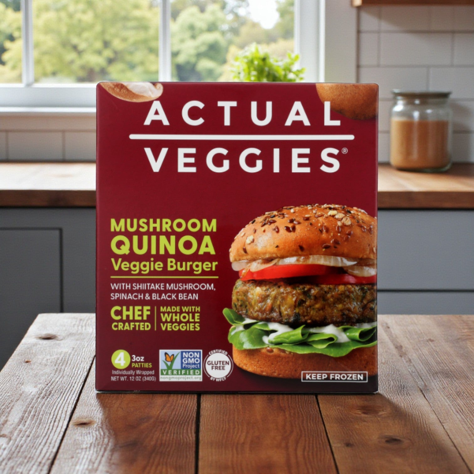 A box of Actual Veggies Gourmet Veggie Burger 3-Pack—featuring Super Greens, Mushroom Quinoa & Black Bean varieties—is displayed on a kitchen counter, highlighting gourmet burgers and product details on the front.