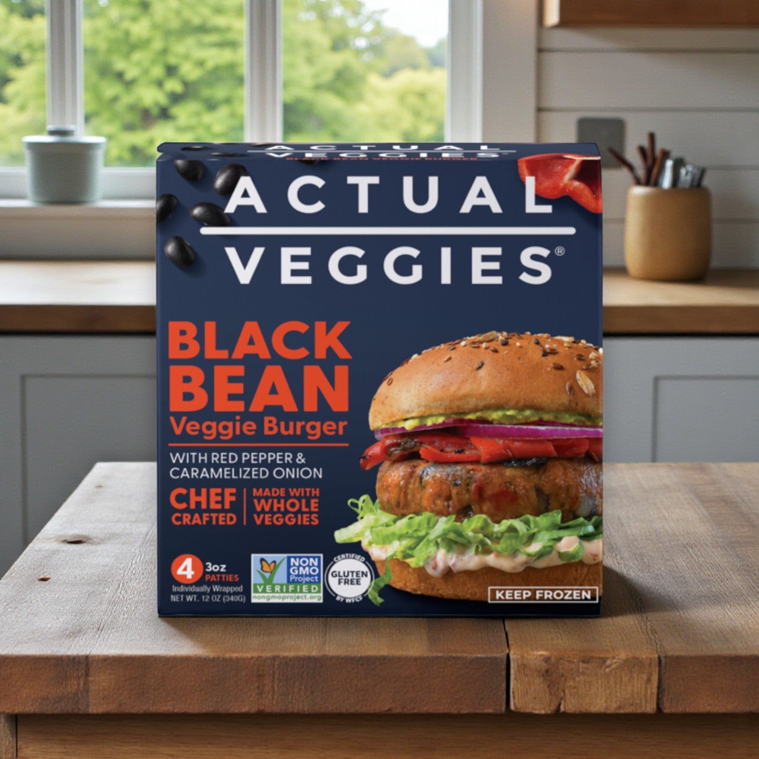 A box of Actual Veggies Gourmet Veggie Burger 3-Pack – Super Greens, Mushroom Quinoa & Black Bean (4 x 3 oz each) from Actual Veggies sits on a wooden kitchen counter, displaying gourmet plant-based burgers and product details on the front.