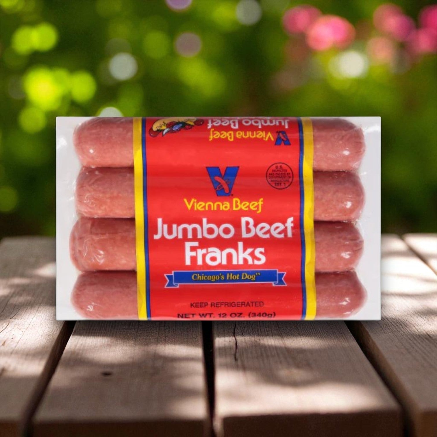 A package of Vienna Beef Jumbo Beef Franks – 12 oz, 4 Count (1 Case) from Vienna Beef rests on a wooden surface with a blurred green and pink outdoor background, perfect for making classic Chicago-style hot dogs.