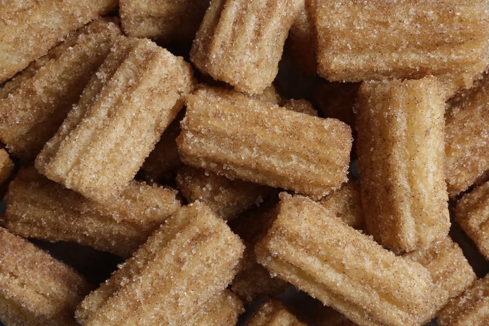 A close-up view of several mini churros coated in cinnamon sugar, showing their ridged texture and golden-brown color.