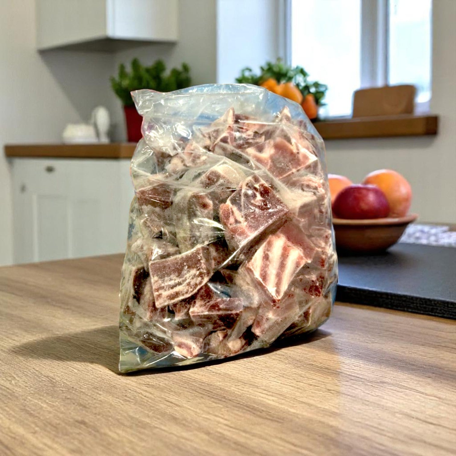 A plastic bag of marbled chocolate pieces sits on a wooden kitchen counter next to Restaurant Depot’s Halal Goat Cubes-15lbs-1 Case (Frozen), with fruit and herbs in the background.