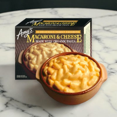 A box of Amy's Macaroni & Cheese-1 Count by Amy's and a serving of the dish, rich with creamy cheddar cheese, in a brown bowl on a marble surface.