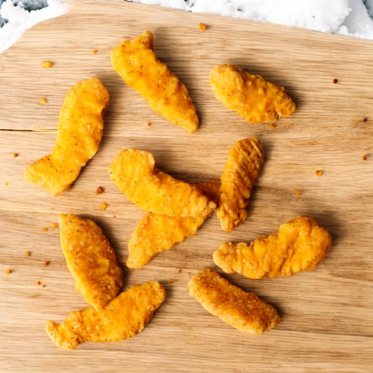 On a wooden surface lies a scattering of Applegate Gluten Free Breaded Chicken Breast Tenders, with each of the eight pieces offering a delicate hint of honey and maple flavor.