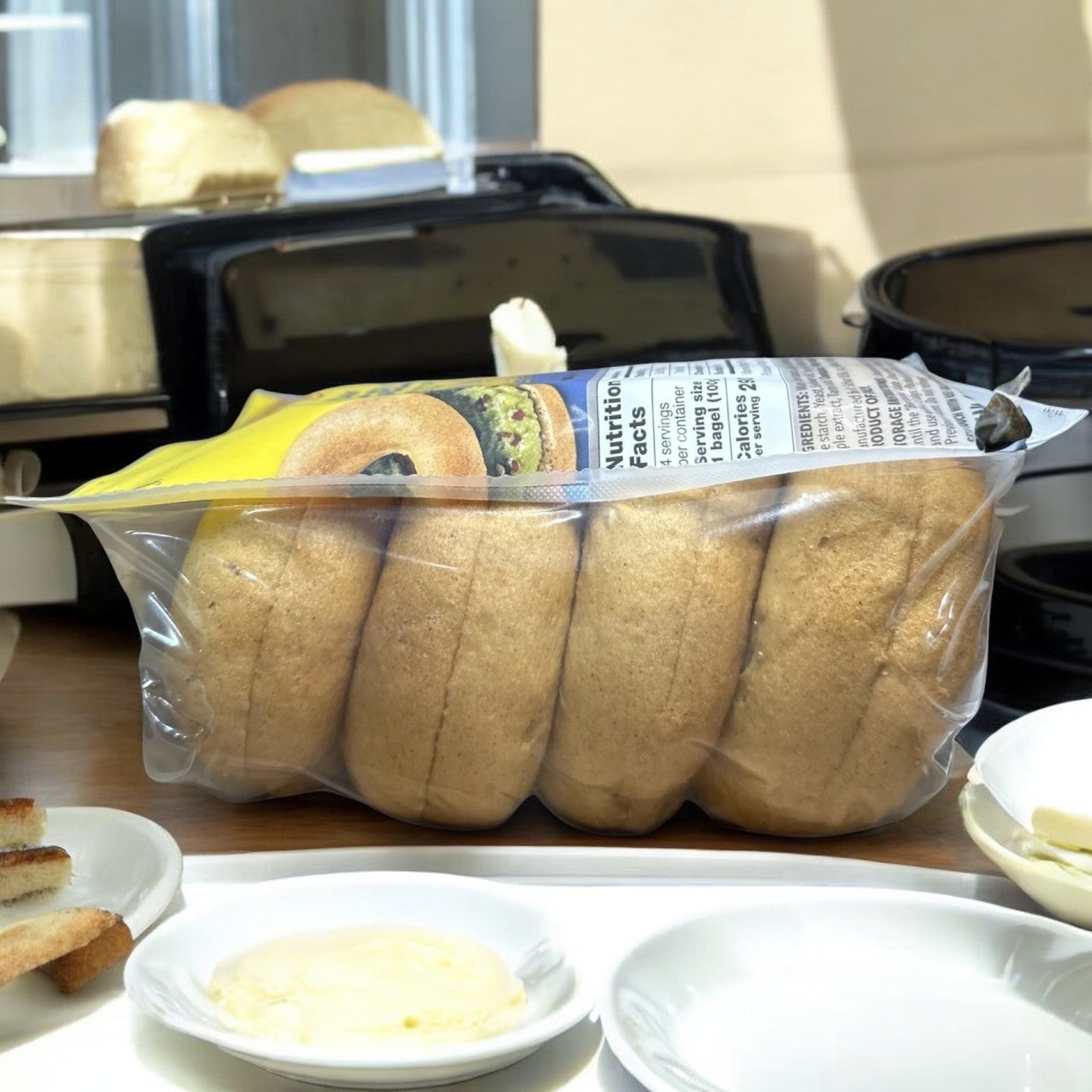 A bag of Schär New York Style Gluten-Free Bagels is on the table alongside plates with butter and toast slices.