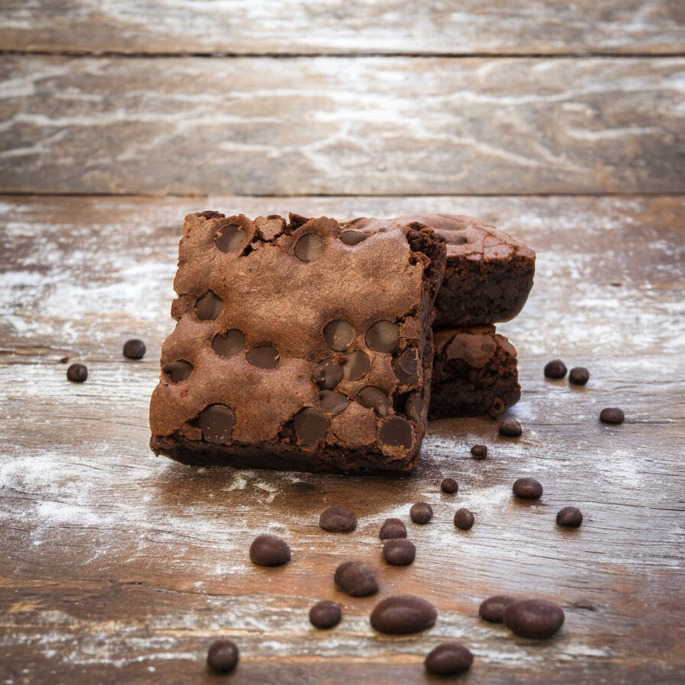 Two David's Cookies Gluten-Free Individually Wrapped Chocolate Chip Brownies, stacked on a wooden surface and surrounded by scattered coffee beans, offer a tantalizing treat.