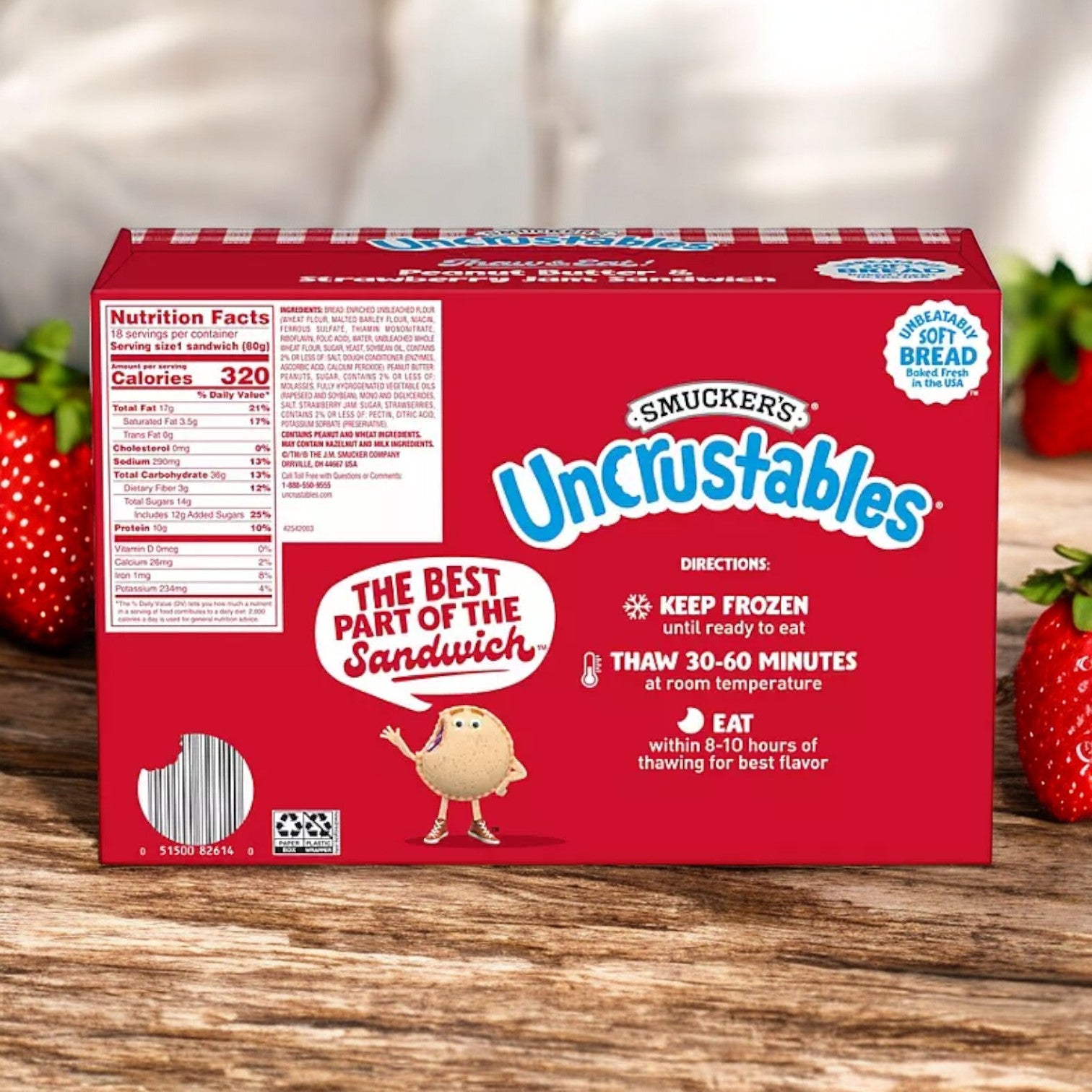 A box of Uncrustable Smuckers Peanut Butter and Strawberry Jam Sandwiches 50.4 oz, 18 Pack features red packaging with nutritional facts and instructions to keep frozen, thaw for 30-60 minutes, and consume within 6-10 hours. The delectable peanut butter and strawberry jam filling serves as a perfect treat. Strawberries are depicted in the background.