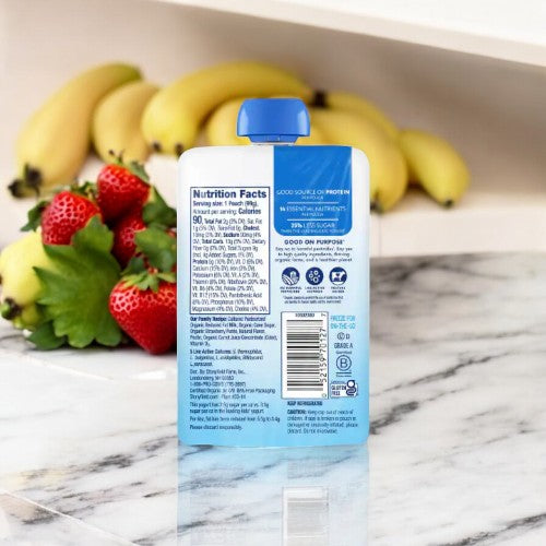 Back view of a Stonyfield Yogurt Strawberry Banana Pouch with nutritional information on a marble counter, alongside fresh strawberries and bananas in the background, perfect for a protein snack from Stonyfield's.