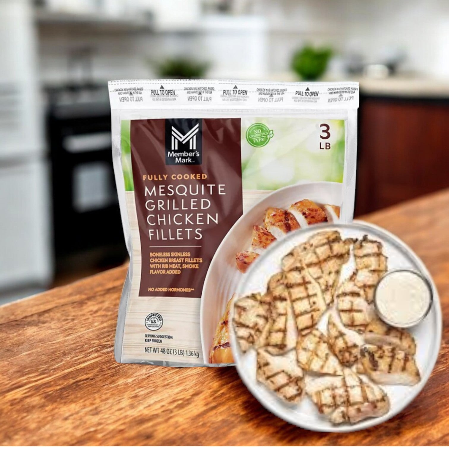 A package of Member's Mark Mesquite Grilled Chicken Breast (3 lbs) sits invitingly beside a plate of sliced chicken with dipping sauce on a kitchen counter.