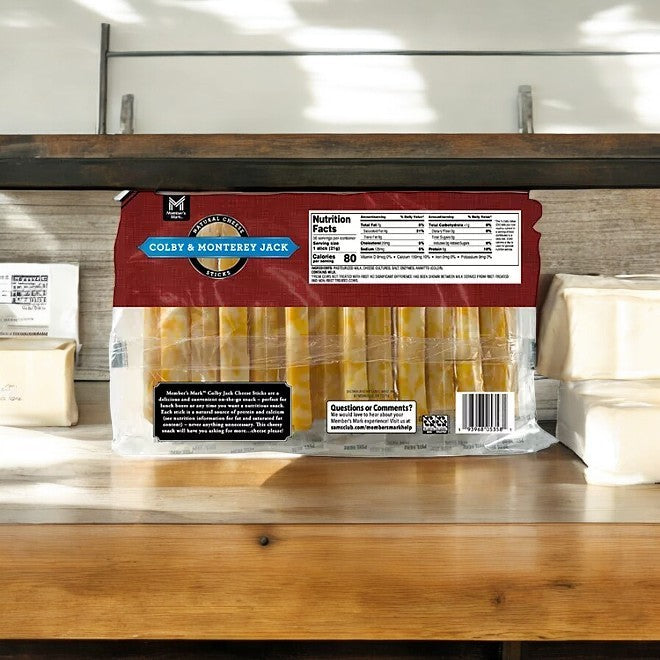 A pack of Easy Lunches Member's Mark Colby and Monterey Jack Cheese Sticks, 36 ct—3 Packs, sits on a wooden shelf next to cheese blocks. The visible nutrition label highlights this as a perfect grab-and-go snack for cheese lovers.