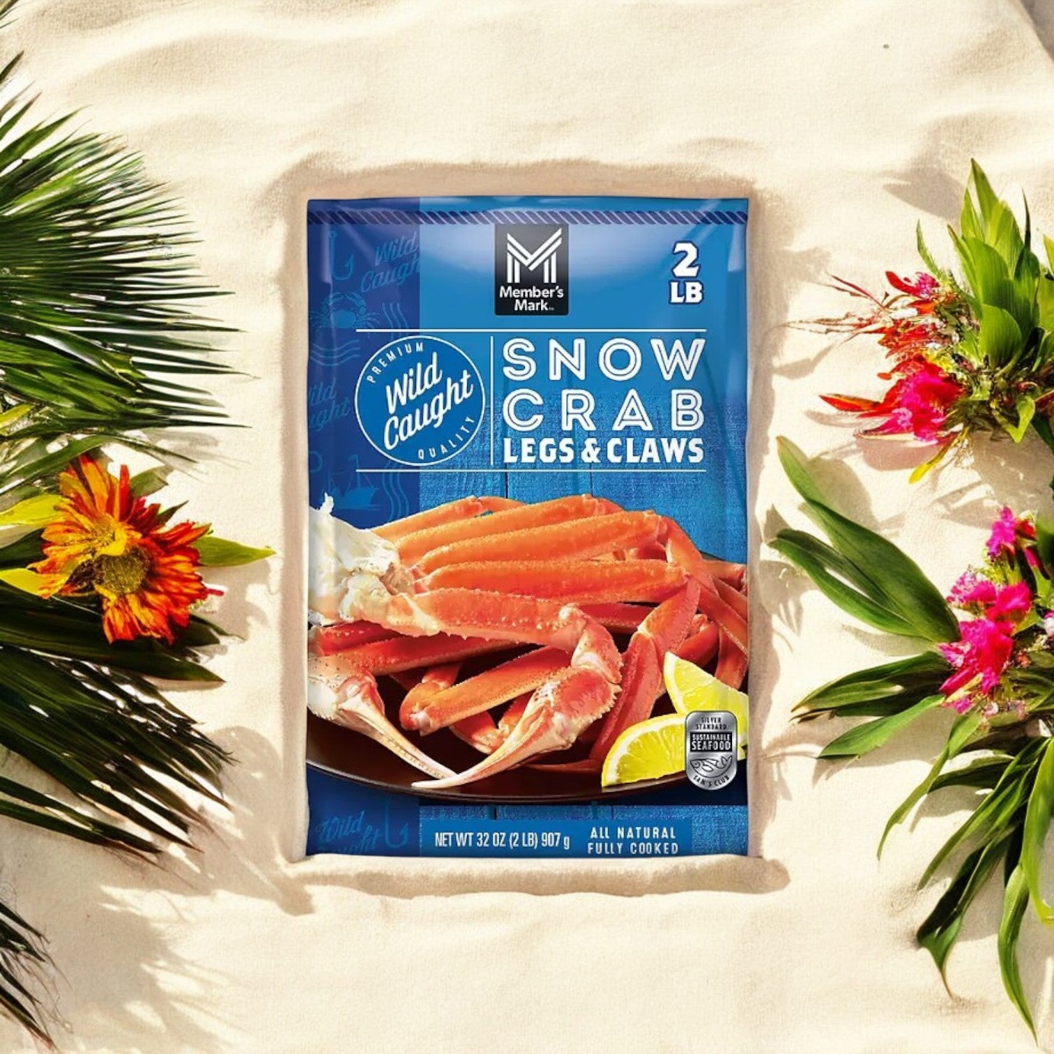 Member's Mark Wild Caught Snow Crab Legs and Claws, 2 lbs., are beautifully presented on sand with vibrant tropical flowers and leaves, creating a delicious and visually stunning seafood feast.