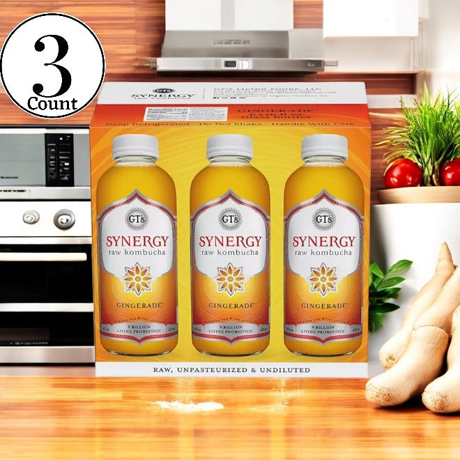 A package containing three GT's Organic Raw Kombucha Gingerade bottles, attractively positioned on a kitchen counter alongside fresh ginger root and a small plant, offers a revitalizing boost to your daily routine with its rich probiotic content.