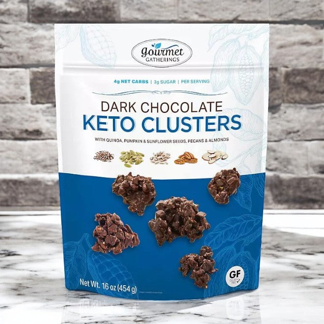 A 16 oz bag of Member's Mark Gourmet Gatherings Dark Chocolate Keto Clusters features a sugar-free mix of quinoa, seeds, pecans, and almonds. Ideal for a keto diet, its packaging showcases detailed nutritional information.