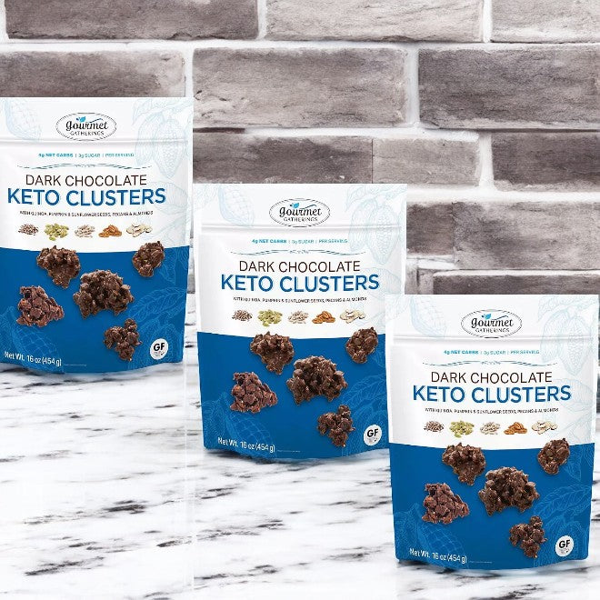 Three packages of Member's Mark Gourmet Gatherings Dark Chocolate Keto Clusters are elegantly displayed on marble against a gray brick background—an ideal sugar-free treat for your keto diet.