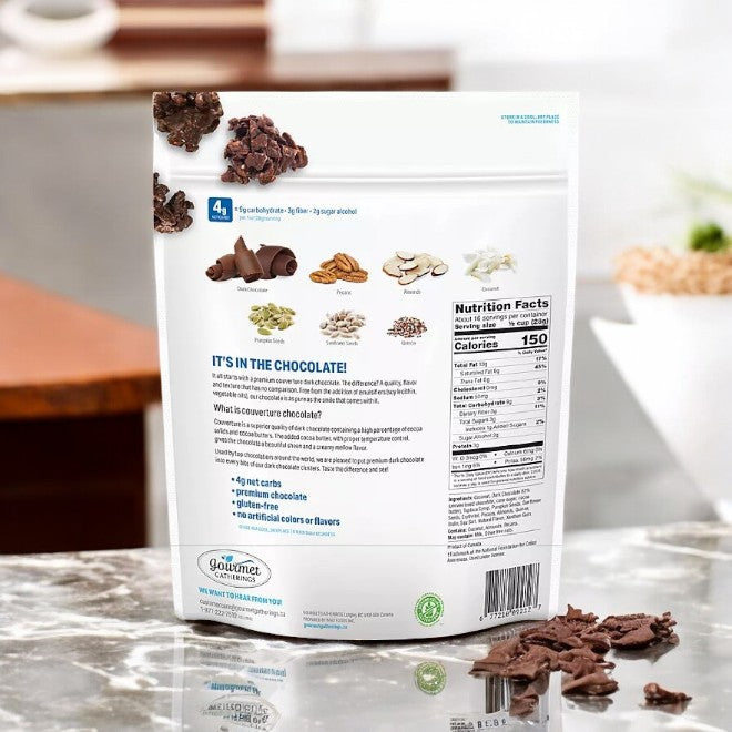 On a kitchen counter, the back of a chocolate package reveals ingredients, nutritional facts, and highlights. Enjoy guilt-free indulgence with Member's Mark Gourmet Gatherings Dark Chocolate Keto Cluster—ideal for keto dieters seeking a sugar-free snack.