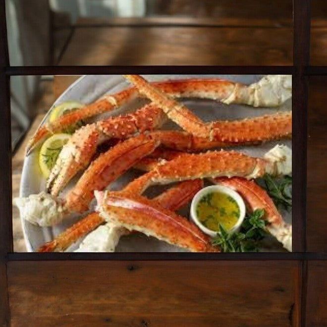 A serving of Aqua Star Wild Southern King Crab Legs and Claws, sourced sustainably, adorned with lemon wedges and accompanied by a small bowl of dipping sauce, graces the wooden table. This premium offering from Aqua Star ensures an indulgent dining experience.