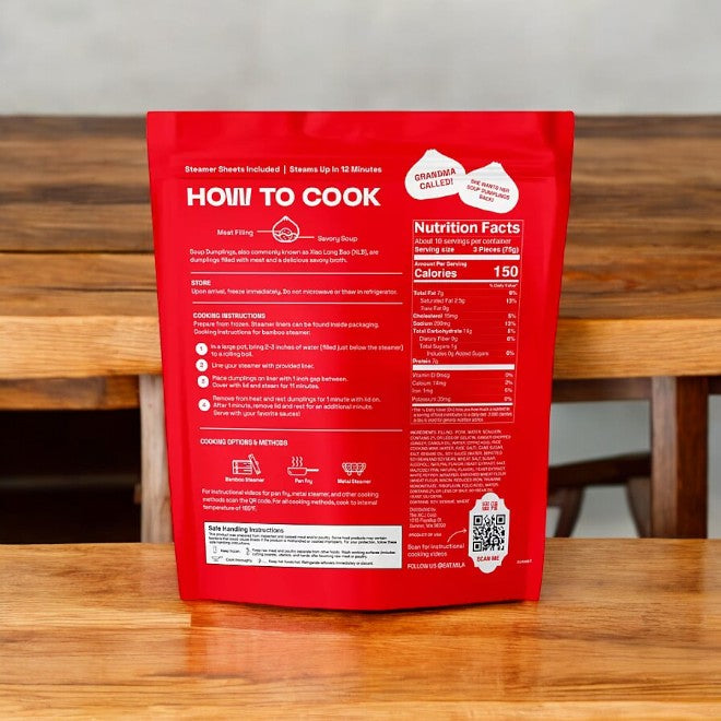 A package of red MiLa Pork Soup Dumplings from Easy Lunches stands on a wooden table. The back displays cooking instructions, nutritional facts, and a QR code.