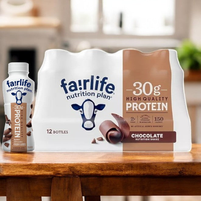 A case of FairLife Nutrition Plan Chocolate Bottles, each 11.5 fl oz, sits on a wooden table with one bottle beside it, showcasing a high-protein drink enriched with 30g of ultra-filtered milk protein in a cozy kitchen setting.