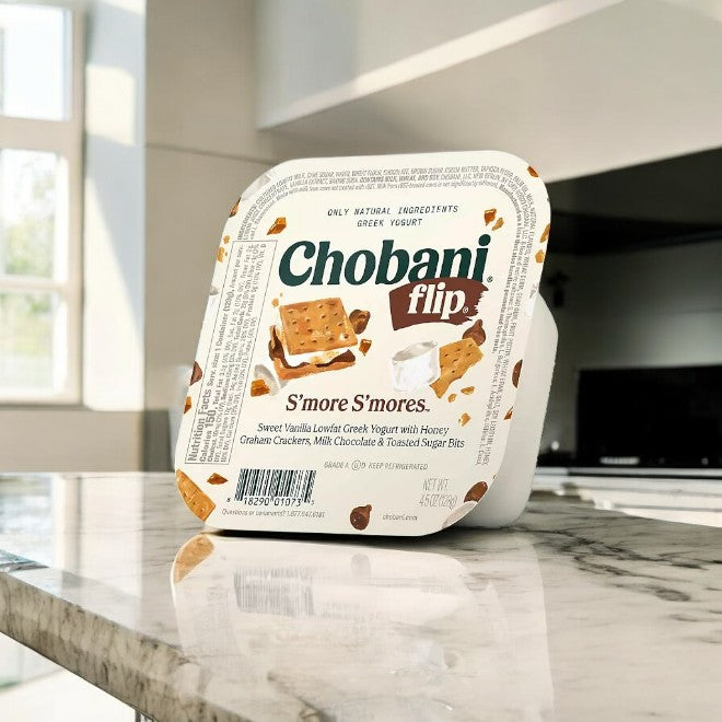 A Chobani Flip Lowfat Greek Yogurt container from the 16-count variety pack rests on a marble countertop in a bright kitchen, providing a tasty twist of creamy indulgence for those who enjoy diverse flavors.