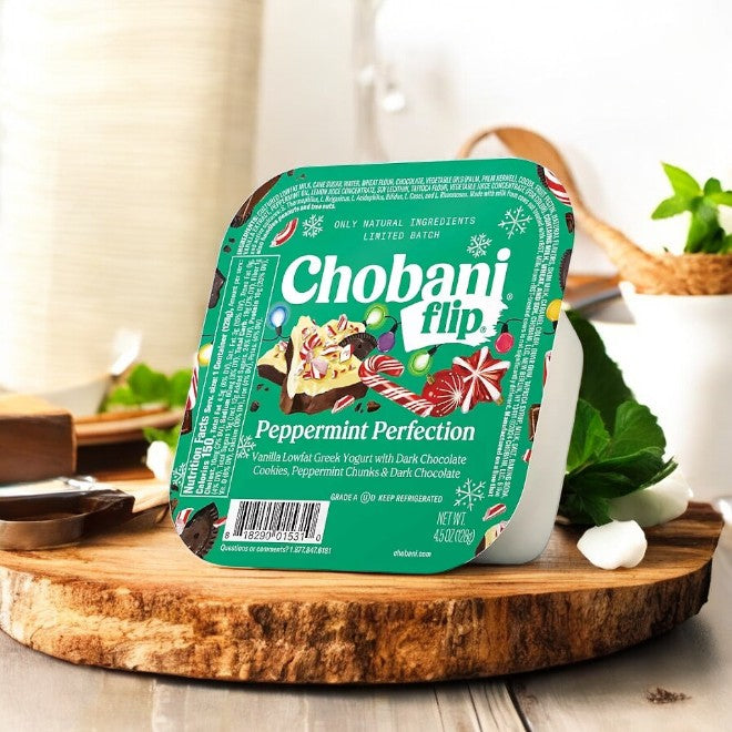 A Chobani Flip Lowfat Greek Yogurt container from the variety pack sits invitingly on a wooden board with its festive "Peppermint Perfection" holiday-themed design.