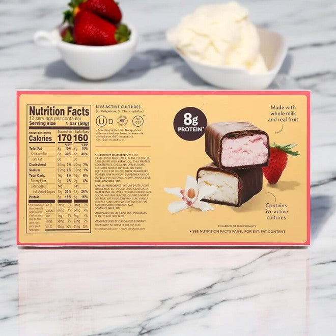 A box of Clio Greek Yogurt Bars, Strawberry & Vanilla, 12 pk-1 Count is shown with nutrition facts displayed. A bowl of strawberries and cream in the background offers a delightful twist to your high-protein snack.