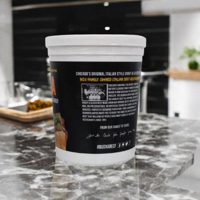 A Buona Italian Sliced Gravy & Italian Beef container rests on a marble countertop in the kitchen, evoking the ambiance of a Chicago-style deli known for its Italian beef dishes.