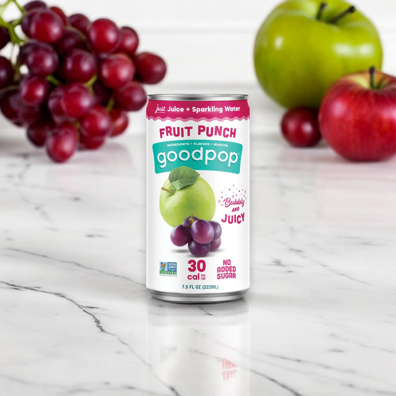 A can of GoodPop Just Juice + Bubbly Water Mini Cans Fruit Punch (7.5 oz) on a marble countertop, surrounded by grapes, a green apple, and a red apple in the background. The kids' juice can is labeled with "30 cal," "No Added Sugar," and offers refreshing sparkling water.